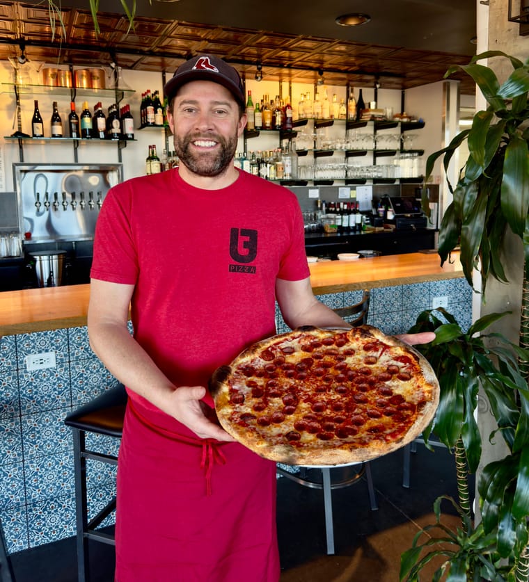 Owner of Urban Field Pizza & Market holding a fresh pepperoni pizza